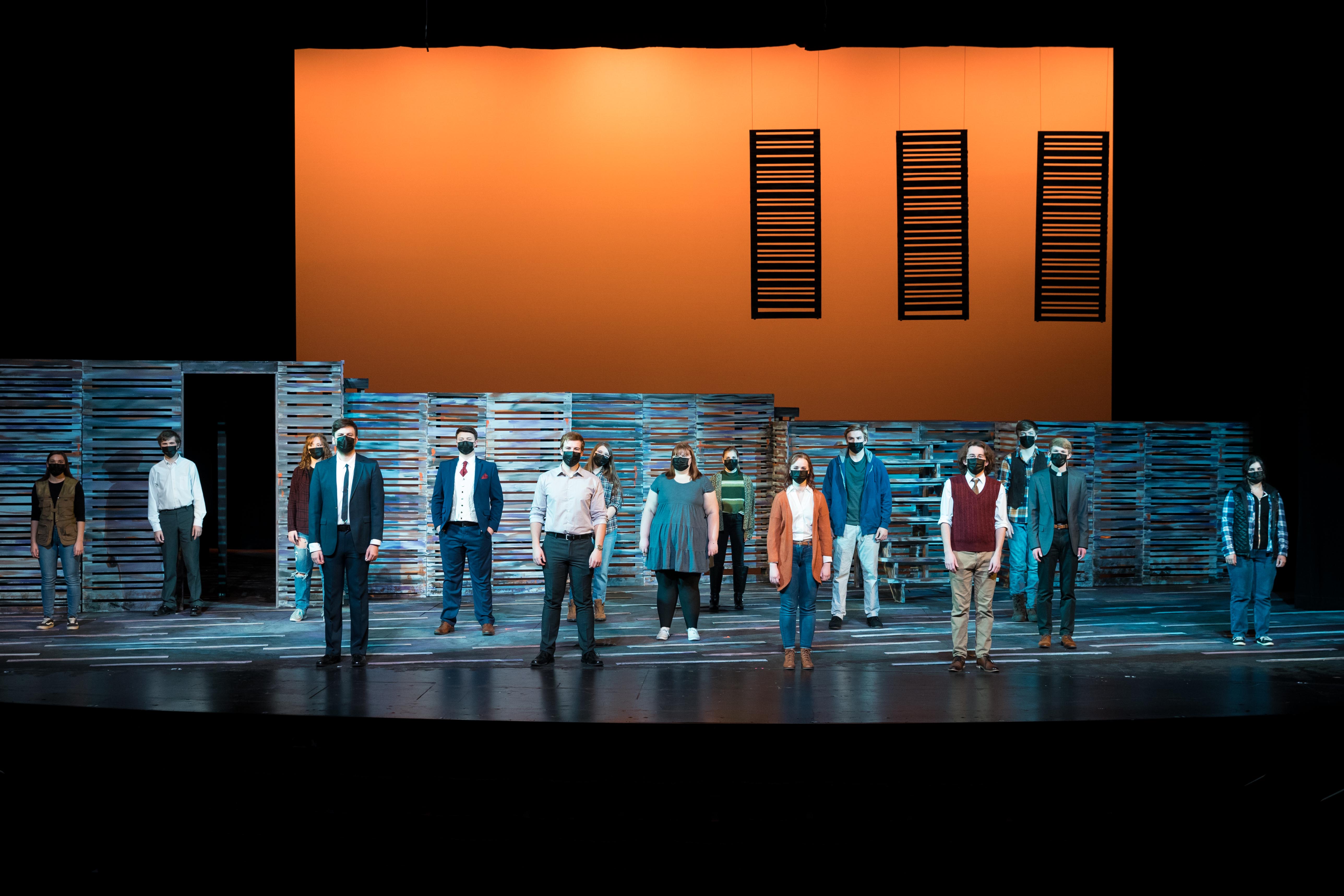 The cast of South Dakota State University's production of The Living, equally spaced on a stage under orange lighting.