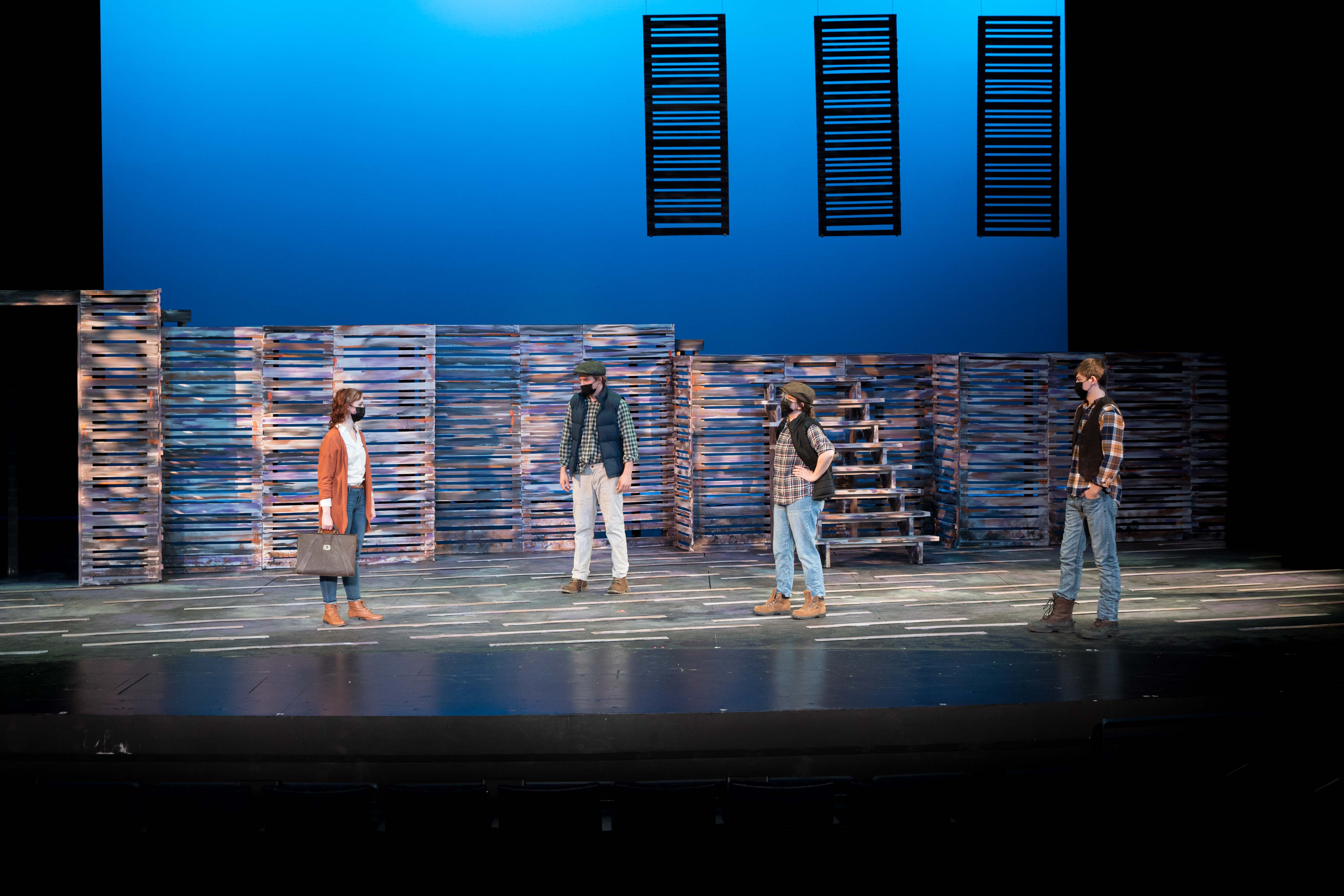 Four people on a stage under blue light, one holding a bag.