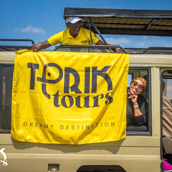 Man on safari vehicle holding 'TPRIK tours' banner, woman looking out window