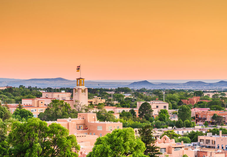 Town with adobe-style buildings, tower, and mountains at sunset