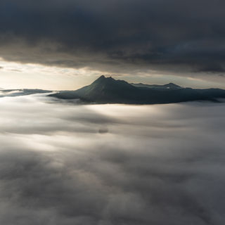 北海道弟子屈町の摩周湖第3展望台から望む夜明けの雲海。厚い雲の隙間から光が差し込み、霧に包まれた摩周岳（カムイヌプリ）を照らし出している幻想的な風景。