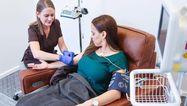 Nurse administering treatment to a patient in a comfortable chair, with a blood pressure monitor visible, in a modern medical setting.