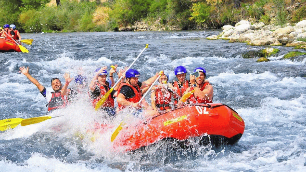 A group of international tourists navigating the white-water rapids of Köprülü Canyon on an inflatable raft, surrounded by stunning cliffs and pine forests, on a guided adventure by Turcome departing from Alanya.