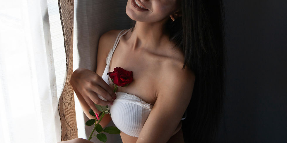 Una donna a una finestra che sorride in reggiseno bianco che tiene una rosa sul petto