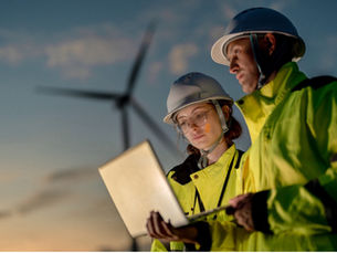 Two people looking at data on laptop in front of wind turbines
