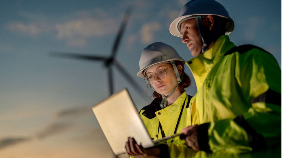 Two people looking at data on laptop in front of wind turbines