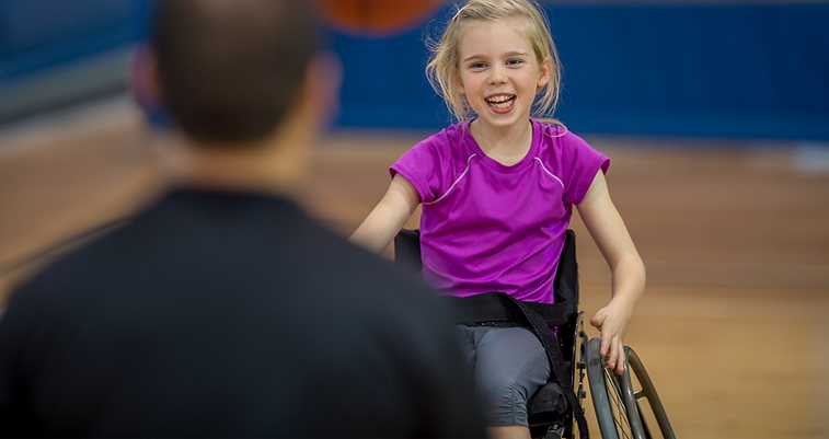 Young disabled girl in wheelchair smiling in sports hall with coach