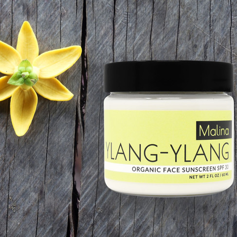 Yellow flower and Malina Ylang-Ylang sunscreen jar on a rustic wooden surface, evoking a natural and organic vibe.