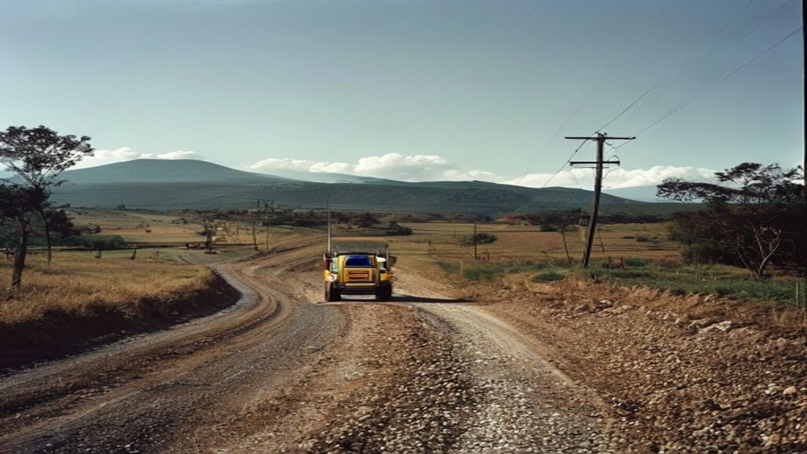 Estrada de chão cascalhada no interior do Rio Grande do Sul com patrol/máquina ao fundo, paisagem rural, sem rostos identificáveis — Cristal