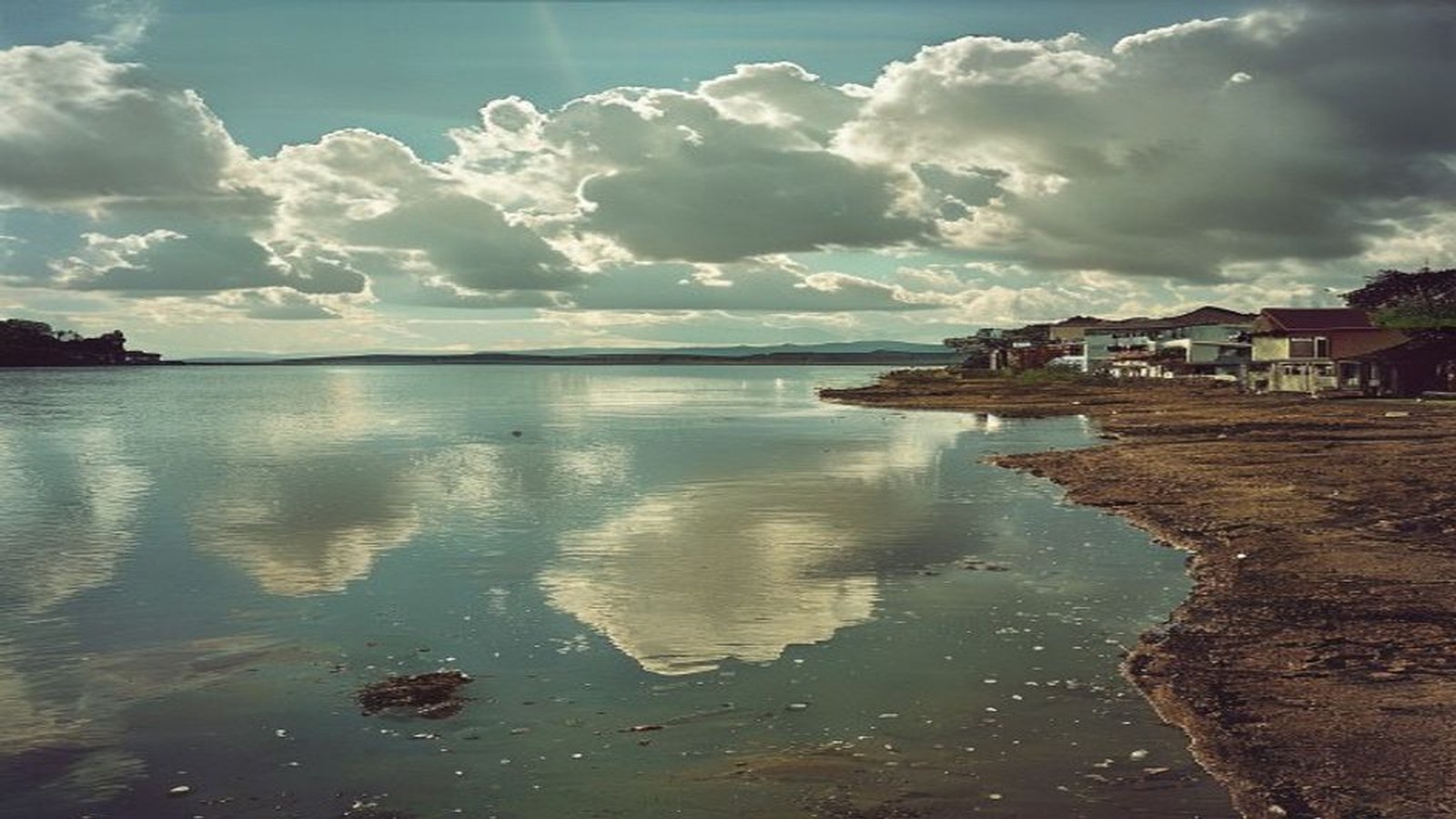 Vista da orla da Lagoa dos Patos em São Lourenço do Sul com céu de sol entre nuvens, sem pessoas