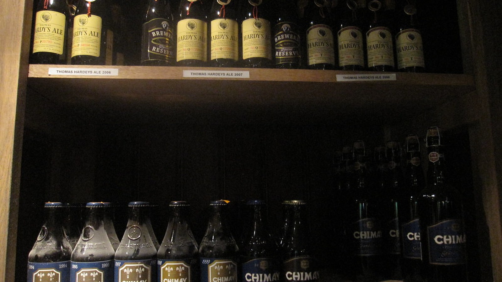 Garrafas de vinho empoeiradas em prateleira de mercado, foco nas garrafas antigas, sem marcas legíveis nem pessoas — vinhos vencidos, RS
