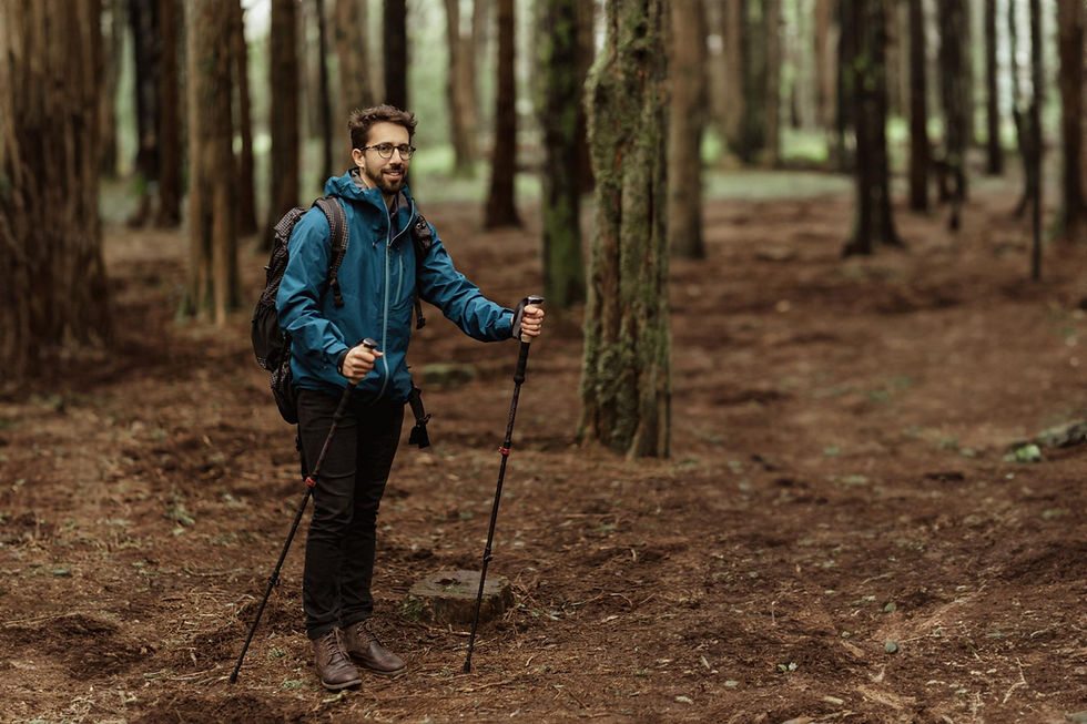Person wearing synthetic active wear is hiking through a forest with a pair of hiking poles.