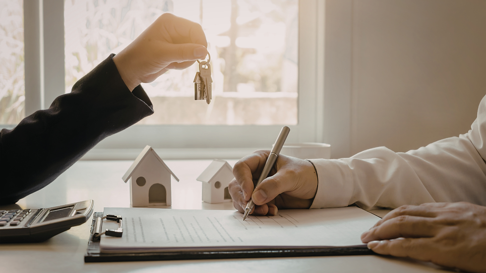 Hand holding keys, passing to another signing documents with a pen. Mini house models and calculator on table. Bright background.
