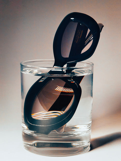 Schwarze Sonnenbrille in einem klaren, mit Wasser gefüllten Glas.