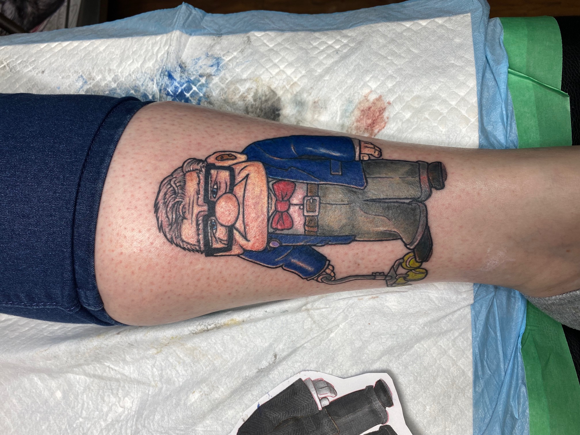 Colour cartoon figure tattoo photographed on a client's lower leg with no face visible
