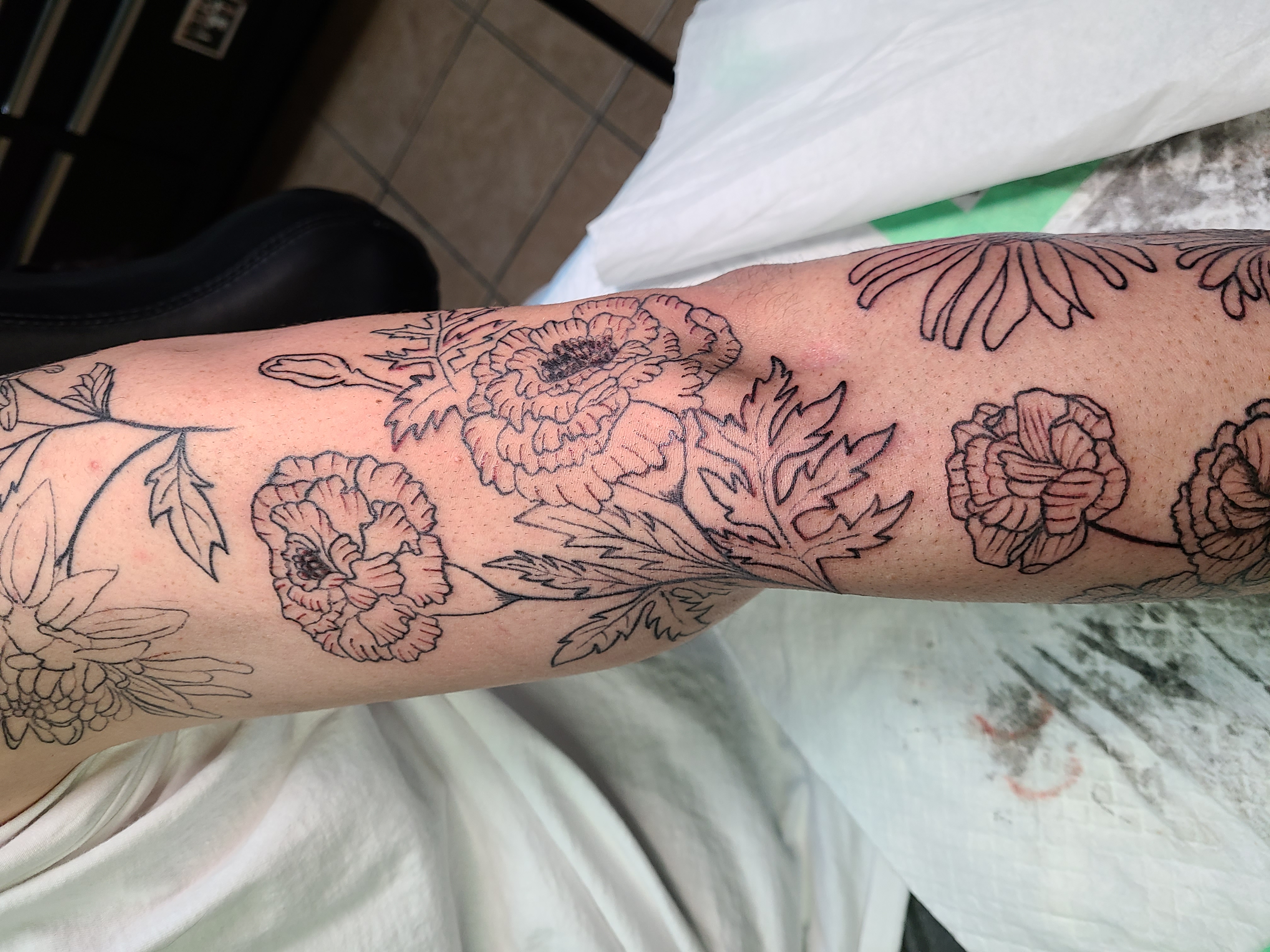 Black floral linework tattoo photographed on a client's upper arm with no face visible