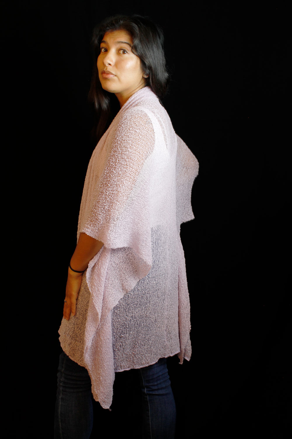 Side back view of model in jeans & white blouse with sheer white open shawl-like jacket