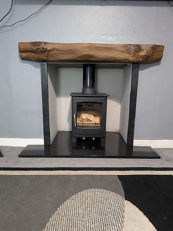 A modern fireplace with a black wood-burning stove set against a gray wall. A rustic wooden mantel and a sleek black base add warmth and style