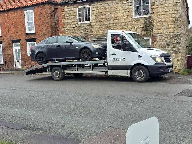 Silver car being towed onto a flatbed truck in a suburban driveway.
