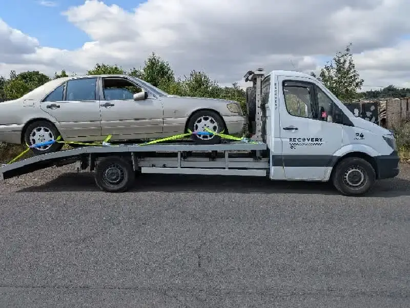 A small silver car being loaded onto a flatbed tow truck on a residential street.