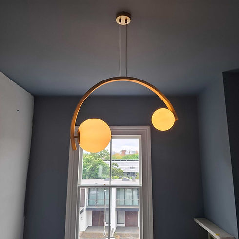 Stylish arched brass pendant chandelier light with two glowing glass globes hanging indoors