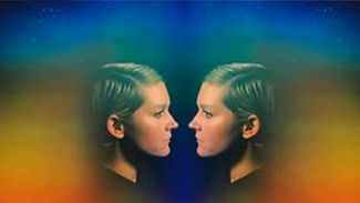 A mirrored portrait of a woman in profile, facing herself, with soft rainbow-colored bands around her head and shoulders to imitate an aura.