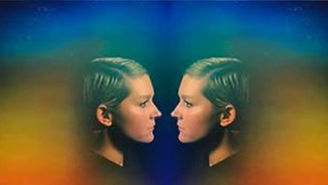 A mirrored portrait of a woman in profile, facing herself, with soft rainbow-colored bands around her head and shoulders to imitate an aura.
