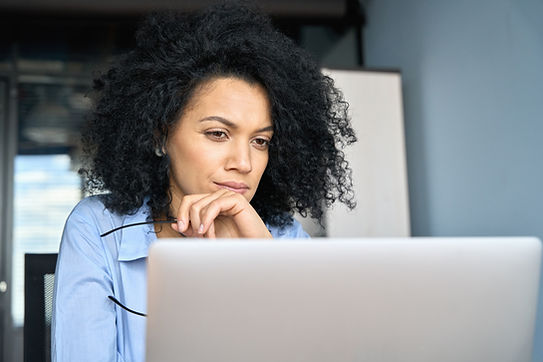 Young serious concerned African American businesswoman sitting at desk looking laptop comp