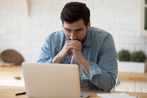 Head shot thoughtful businessman in eyewear looking at computer screen, sitting at table a