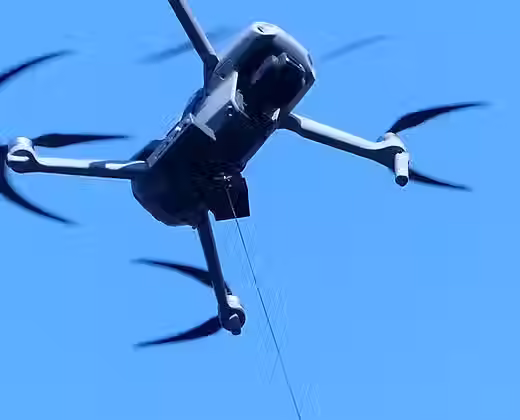 A DJI mavic AIR 2 is seen hovering in the sky with a payload release and drop accessory from drone sky hook attached to it