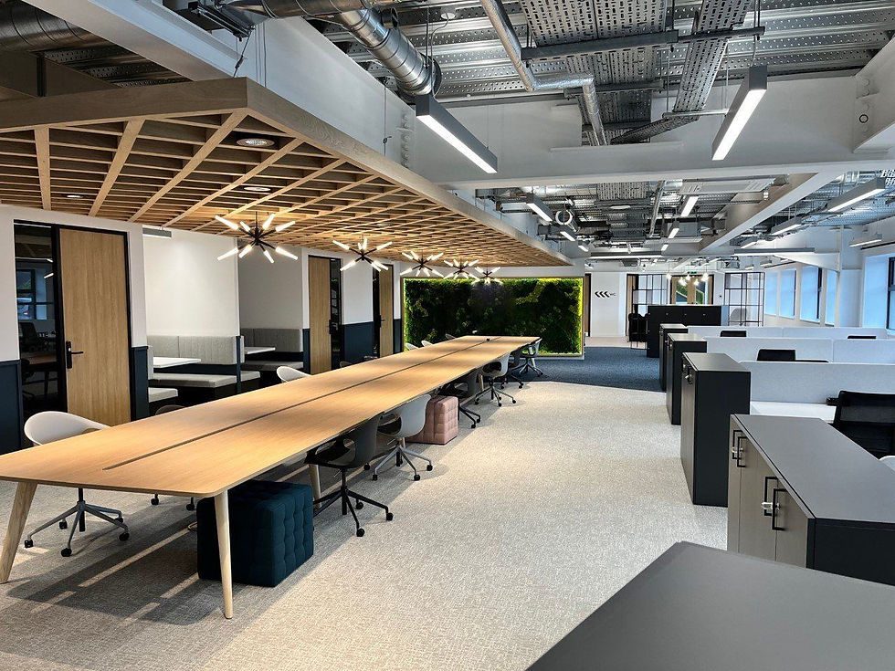 Modern office space with long wooden desks, chairs, and gray cabinets. Overhead lights hang from an exposed ceiling; green wall decor by Rriddhi Siddhi properties