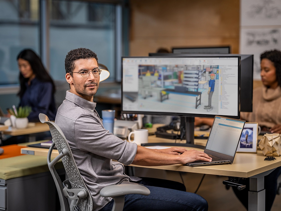 Man at desk working on computer, CAD software on screen. Office setting with plants and soft lighting. Focused mood.
