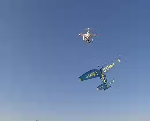 A DJI phantom done is seen carrying a prop plane with a release and drop mechanism from drone sky hook attached to it