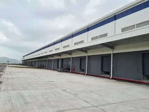 Long industrial warehouse with closed loading docks and a cloudy sky. The building is white and gray with blue accents. Quiet atmosphere.