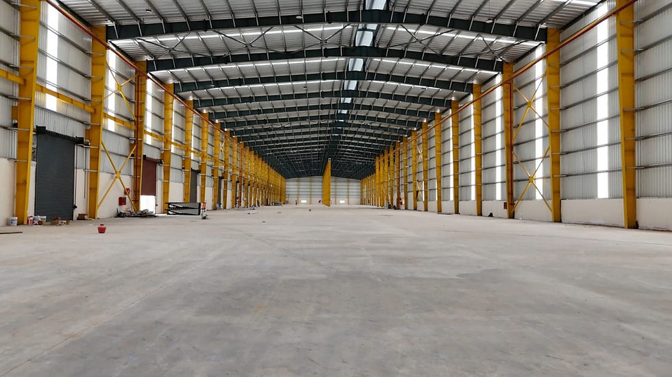 Spacious empty warehouse interior with yellow steel beams, concrete floor, and high metal roof. Bright light streams in, creating a sense of openness.