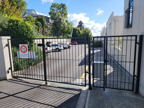 Black metal traffic and pedestrian security gates installed at a commercial premises. Street-facing.