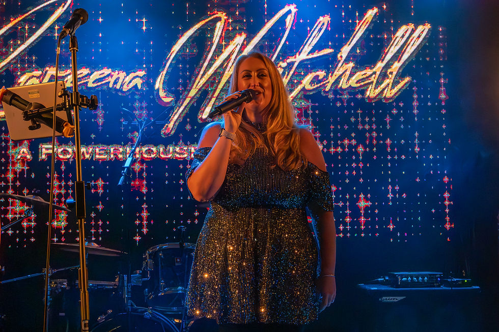 A female singer in a sparkling dress singing into the microphone while stood in front of her name in lights.