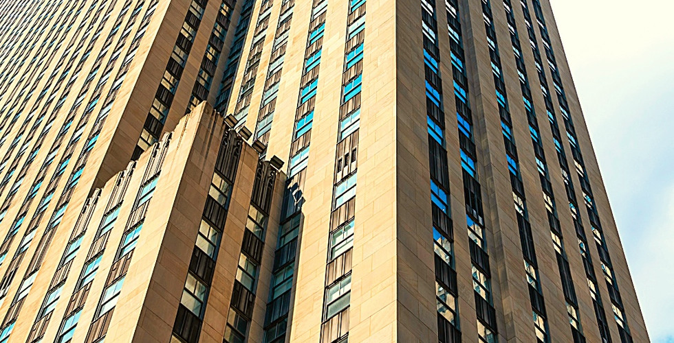 Tall skyscraper under a blue sky, beige facade with many windows. Text reads: Rockefeller Center, New York, America. Latitude, Longitude noted.