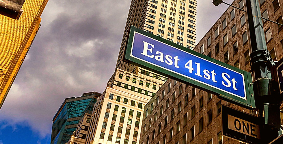 Chrysler Building under cloudy sky, viewed from East 41st St. Sign and streetlamp in foreground, warm sunlight on skyscraper.