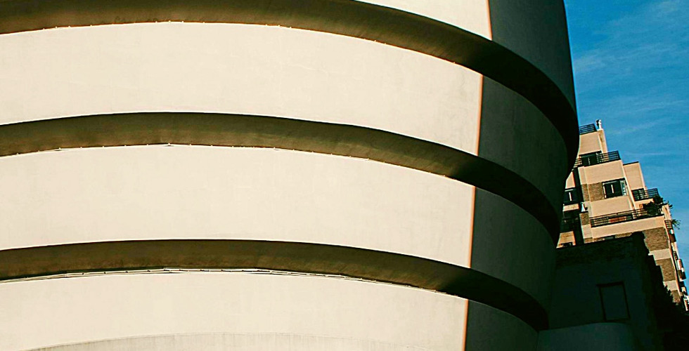 The Guggenheim Museum's curved white facade against a blue sky, with a shadow and a "One Way" sign. Text: Solomon R. Guggenheim Museum.