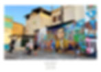 People play basketball in front of a colorful mural on a city street. The mural features vibrant portraits and scenes. Clear blue sky.