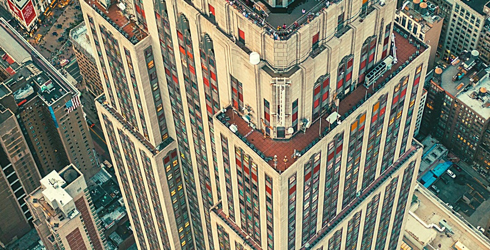 Aerial view of the Empire State Building with beige and red facade, surrounded by densely packed city buildings in New York City.