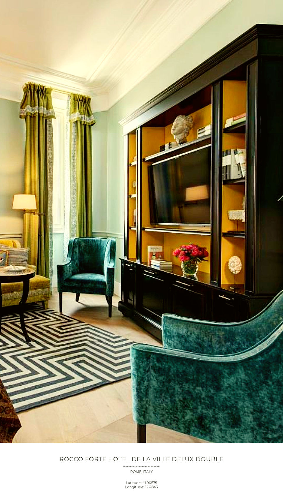 Elegant hotel room with teal chairs, a black TV cabinet, and a geometric rug. Green curtains, art pieces, and a vase of red flowers enhance decor.