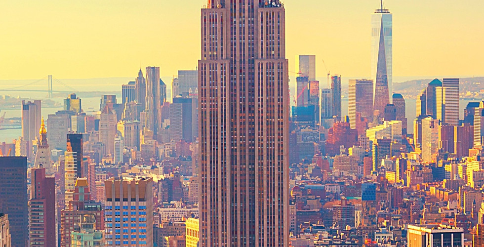 Empire State Building at sunset with city skyline in the background. Warm golden hues. Text at bottom reads "Empire State Building."