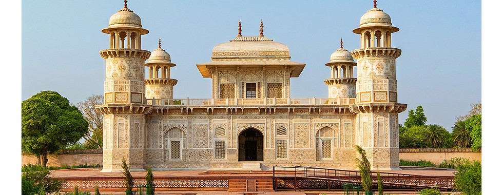 Ornate white mausoleum in Agra with intricate carvings, four minarets, set in a lush garden under a clear blue sky. Text: Agra coordinates.