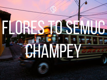A colourful bus speeds through a cobblestone street at sunset. Text reads "FLORES TO SEMUC CHAMPEY." The sky is a vivid pink and purple.