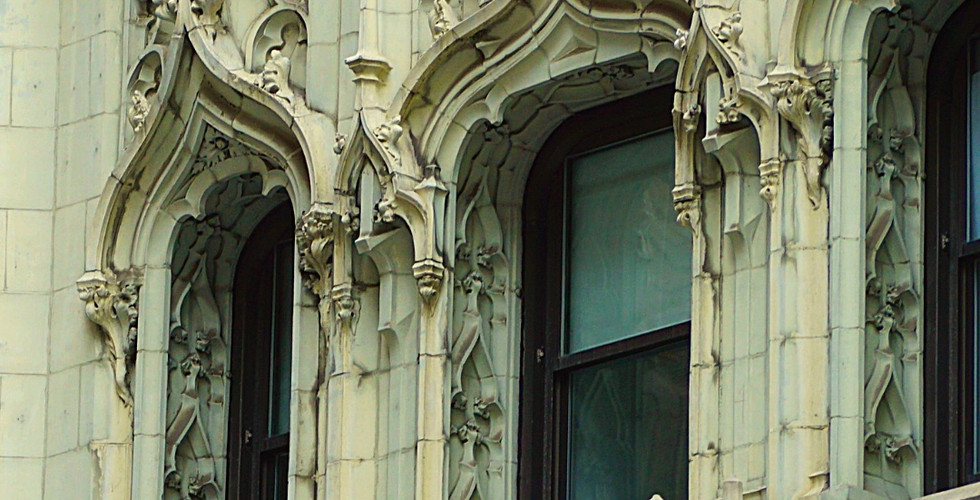 Ornate stone facade of the Woolworth Building with intricate arches and carvings, featuring large windows. Text: "Woolworth Building, New York".