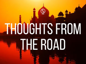 Silhouette of a historic building against an orange sunset, with "THOUGHTS FROM THE ROAD" text overlay, reflecting in water.