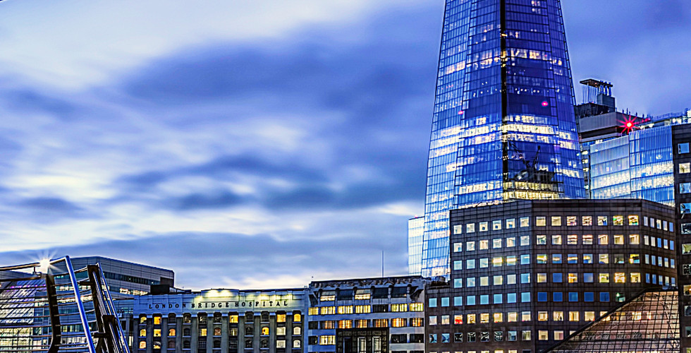 The Shard in London at dusk, illuminated against a cloudy sky. River in foreground, cityscape reflections, and text detailing location below.