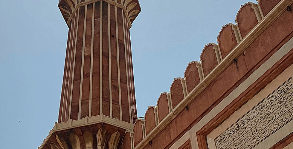 Tall minaret at Jama Masjid, Old Delhi against a clear blue sky. Intricate carvings and arches on red and white architecture.